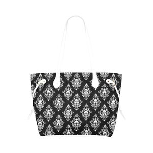 Pu&ograve; includere: Una borsa tote nera e bianca con un motivo damascato bianco che presenta un'immagine ripetuta del viso di Jack Skellington. La borsa ha manici bianchi e lacci di chiusura bianchi.