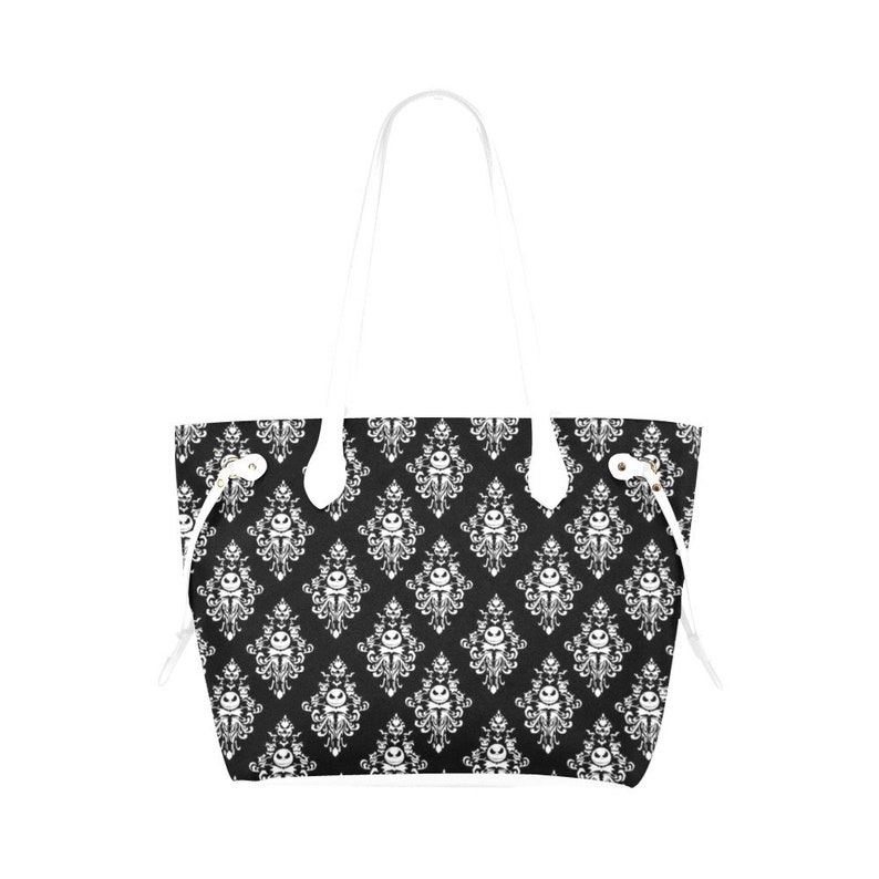 Pu&ograve; includere: Una borsa tote nera e bianca con un motivo damascato bianco che presenta un'immagine ripetuta del viso di Jack Skellington. La borsa ha manici bianchi e lacci di chiusura bianchi.