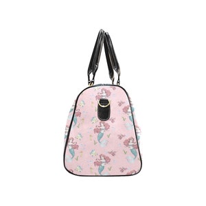 May include: A pink duffel bag featuring a repeating pattern of mermaids with red hair and blue tails. The bag has black handles and trim, with a gold-colored metal ring detail.