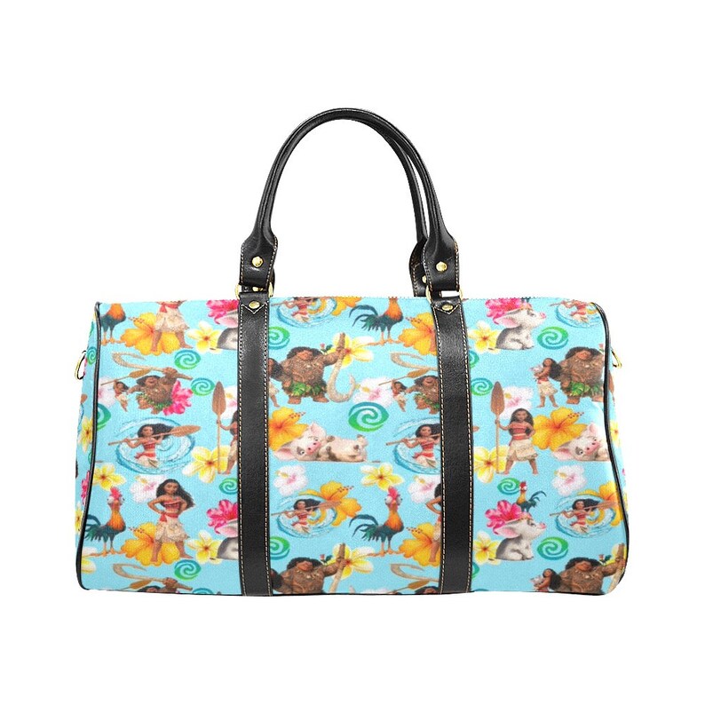 Puede incluir: Una bolsa de viaje azul y amarilla con ribetes de cuero negro y un patr&oacute;n repetido de personajes de la pel&iacute;cula animada Moana. La bolsa tiene dos asas superiores y un cierre de cremallera.