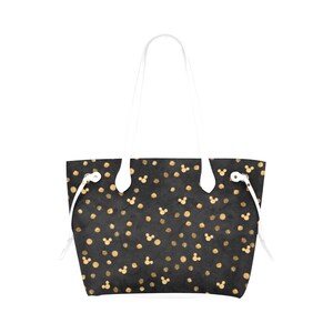 K&ouml;nnte beinhalten: Eine schwarze Tragetasche mit wei&szlig;en Henkeln und einem Muster aus goldenen Punkten und Mickey-Maus-K&ouml;pfen.