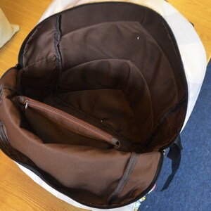 Op de afbeelding: Witte canvas rugzak met een bruin interieur. De rugzak heeft een ritsvak aan de binnenkant.