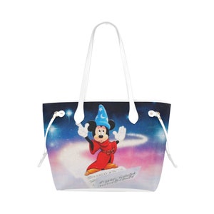May include: White tote bag featuring a colourful image of Mickey Mouse dressed as a sorcerer. Mickey is standing on a sheet of music with a starry night sky background.