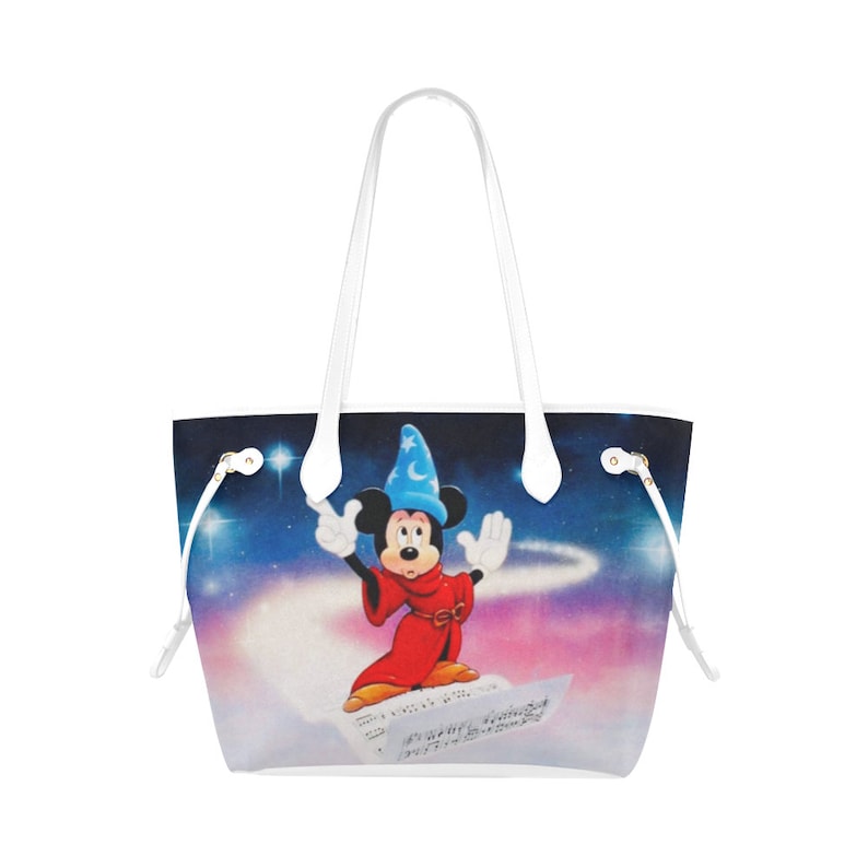 May include: White tote bag featuring a colourful image of Mickey Mouse dressed as a sorcerer. Mickey is standing on a sheet of music with a starry night sky background.