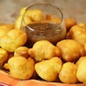 Könnte beinhalten: Eine Schüssel mit goldbraunen frittierten Teigbällchen, serviert mit einer dunkelbraunen Dip-Sauce.