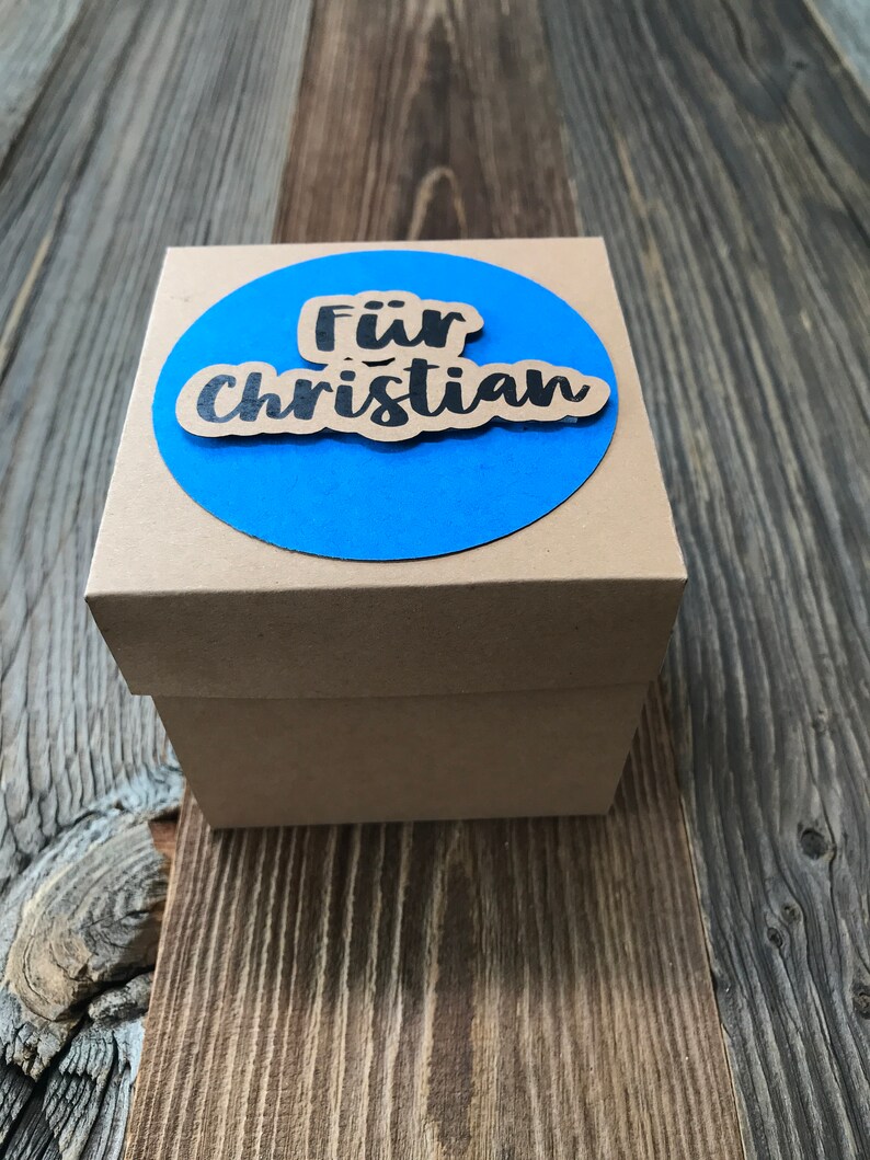 May include: A brown cardboard gift box with a blue circle on top. The circle has the words "F&uuml;r Christian" written in black.