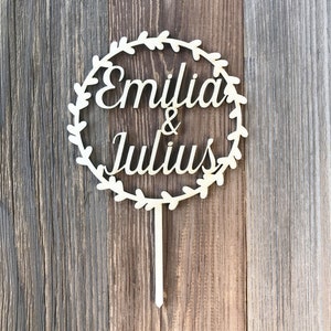 May include: Wooden cake topper with a circle of leaves and the names "Emilia & Julius" in cursive.