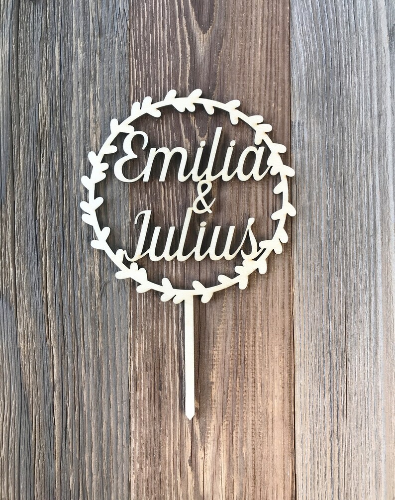 May include: Wooden cake topper with a circle of leaves and the names "Emilia & Julius" in cursive.