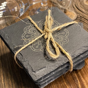 May include: Set of four black slate coasters with a white mandala design. The coasters are tied together with twine.