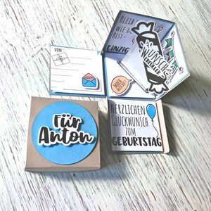 May include: A handmade birthday card with a blue and white color scheme. The card is in a box with the words "F&uuml;r Anton" on a blue circle. The card has multiple panels with German text and illustrations.