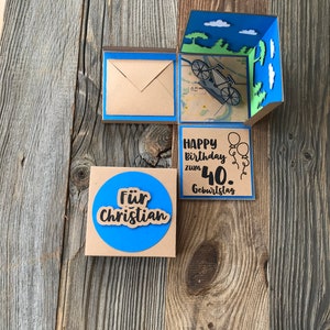 May include: A brown cardboard box with a blue border and a pop-up design. The box has a blue circle with the text "F&uuml;r Christian" and a separate panel with the text "Happy Birthday zum 40. Geburtstag".