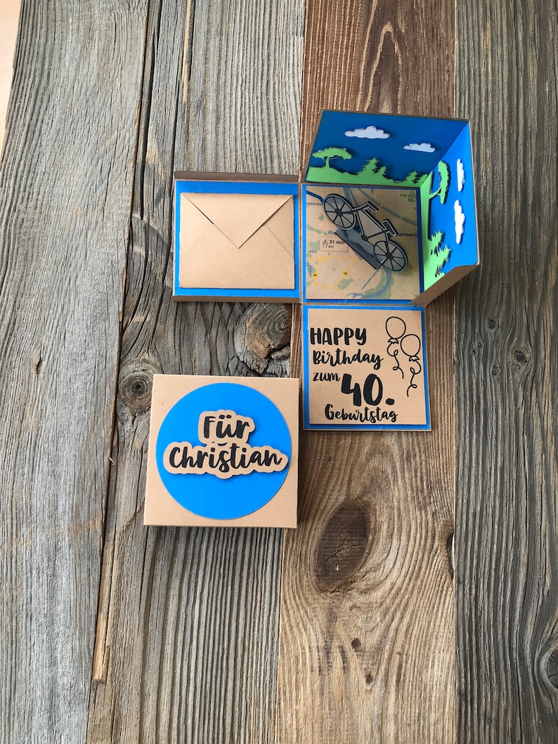 May include: A brown cardboard box with a blue border and a pop-up design. The box has a blue circle with the text "F&uuml;r Christian" and a separate panel with the text "Happy Birthday zum 40. Geburtstag".