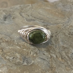 May include: A silver wire wrapped ring with a green stone. The stone has a mottled pattern.