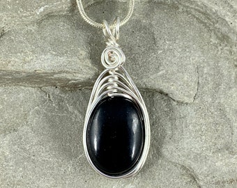 May include: A black gemstone pendant with a silver wire wrap, hanging from a silver chain.