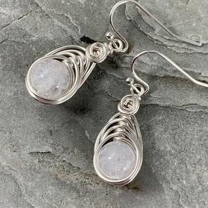 May include: A pair of silver wire wrapped earrings with clear quartz stones. The earrings are teardrop shaped and have a delicate, intricate design.