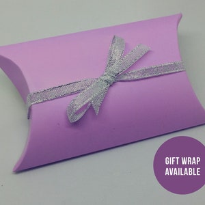 May include: A light purple pillow box with a silver ribbon tied in a bow. The box has the text "Gift Wrap Available" printed on it.