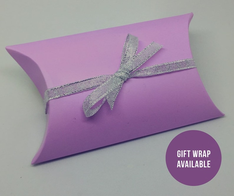 May include: A light purple pillow box with a silver ribbon tied in a bow. The box has the text "Gift Wrap Available" printed on it.