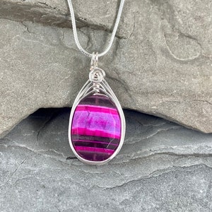 May include: A silver chain necklace with a pink and black agate pendant wrapped in silver wire.