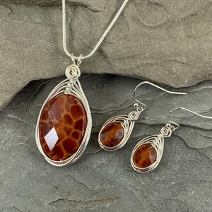 May include: A silver chain necklace and matching earrings with a brown agate pendant and earrings. The agate has a unique pattern that resembles a honeycomb.