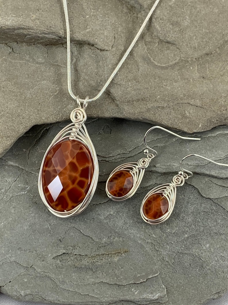 May include: A silver chain necklace and matching earrings with a brown agate pendant and earrings. The agate has a unique pattern that resembles a honeycomb.