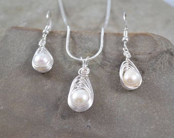 May include: A silver jewellery set comprising a pendant necklace and matching earrings. Each piece features a teardrop-shaped pearl encased in a delicate wire design. The set is displayed on a neutral-toned surface.