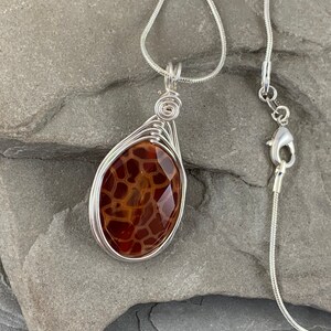 May include: A silver chain necklace with a brown agate pendant wrapped in silver wire.