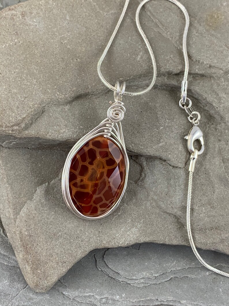 May include: A silver chain necklace with a brown agate pendant wrapped in silver wire.
