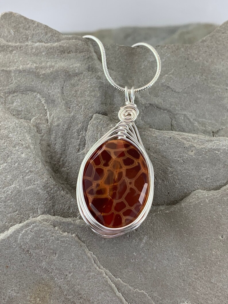 May include: A silver chain necklace with a brown agate pendant wrapped in silver wire. The agate has a unique pattern of brown and white.