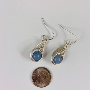 May include: A pair of silver wire wrapped earrings with light blue gemstone beads. The earrings are about the size of a ten pence coin.