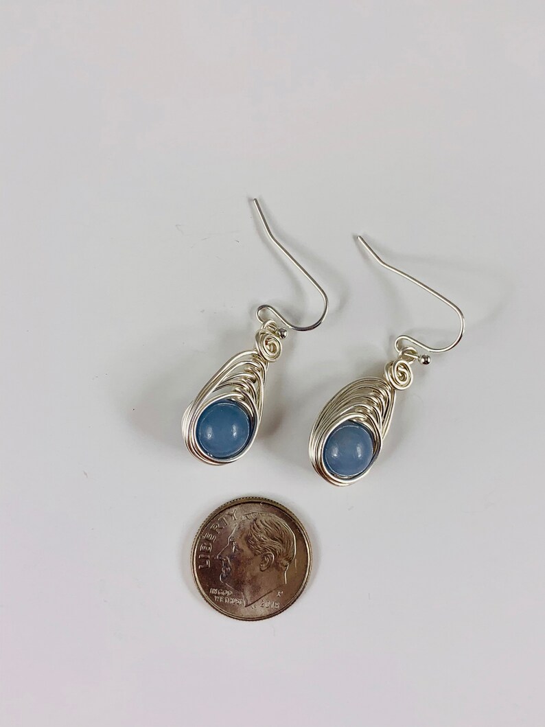 May include: A pair of silver wire wrapped earrings with light blue gemstone beads. The earrings are about the size of a ten pence coin.