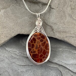May include: A silver chain necklace with a brown agate pendant wrapped in silver wire. The agate has a unique pattern of brown and orange.