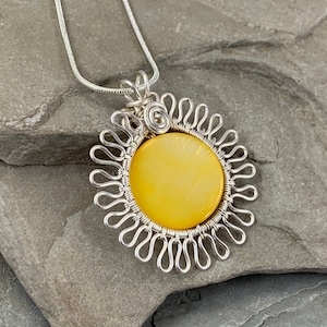 May include: A silver chain necklace with a yellow pendant. The pendant is a circle with a yellow stone in the center and a silver wire design around the edge.