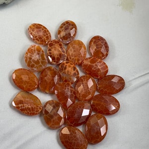 May include: A collection of 15 oval-shaped agate beads with a brown and white pattern. The beads are faceted and have a translucent appearance.