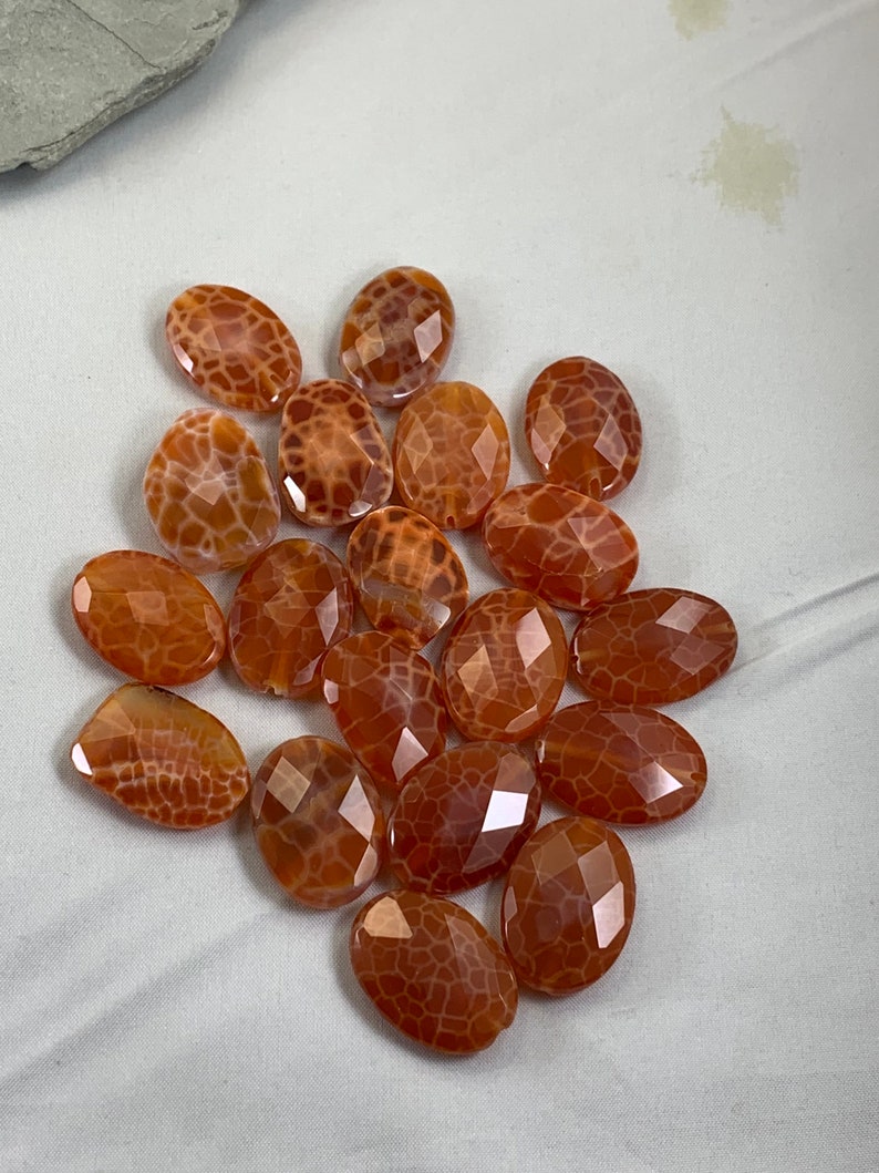May include: A collection of 15 oval-shaped agate beads with a brown and white pattern. The beads are faceted and have a translucent appearance.
