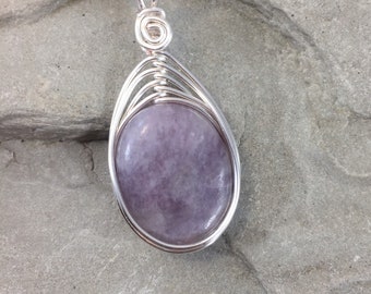 May include: A handcrafted silver pendant necklace featuring a teardrop-shaped design. The pendant has a light purple, oval-shaped stone, encased in a wire-wrapped silver setting. The necklace chain is a silver snake chain.