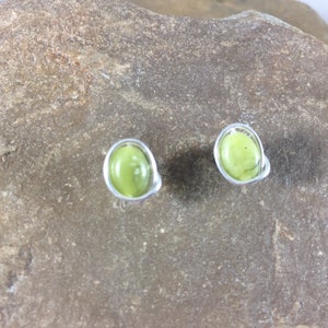 May include: A pair of silver earrings with green stone accents. The earrings are round and have a simple design.