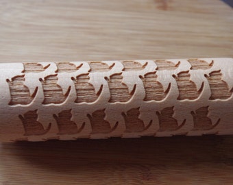 May include: A wooden rolling pin with a repeating pattern of cat silhouettes carved into its surface. The rolling pin is light brown and appears to be made of natural wood. The design is ideal for baking and creating patterned cookies or pastries.
