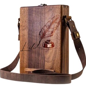 May include: A brown wooden box with a leather strap. The box has a design of a feather and inkwell with the word "Lili" written below it.