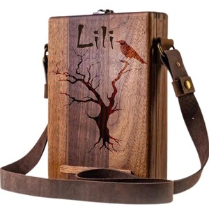 May include: A wooden box with a brown leather strap. The box has a tree and bird design engraved on it. The name "Lili" is also engraved on the box.