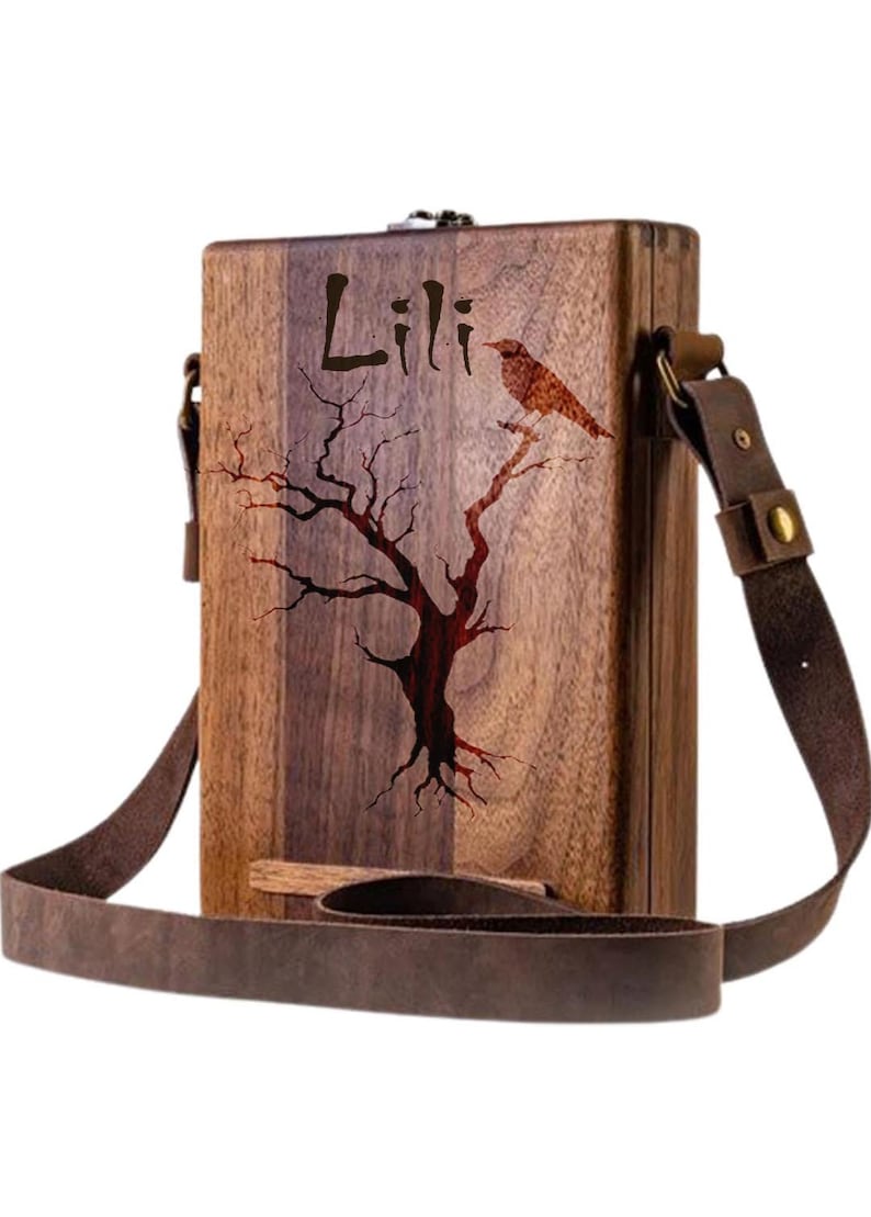May include: A wooden box with a brown leather strap. The box has a tree and bird design engraved on it. The name "Lili" is also engraved on the box.