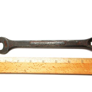 May include: A rusty wrench with a black handle and the word "BARCALO" printed on it. The wrench is 7 inches long and is next to a wooden ruler.