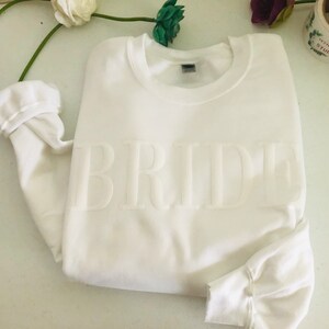 May include: White sweatshirt with the word "BRIDE" in raised lettering.