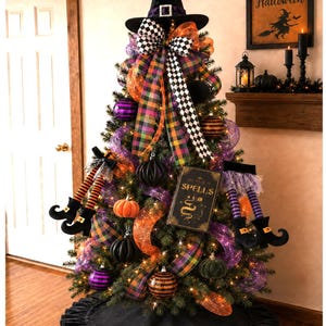 May include: A decorated artificial Christmas tree featuring a black witch hat topper, a book titled The Book of Spells, orange and purple mesh ribbons, plaid ribbons, black and white checkered ribbons, striped witch legs, and pumpkin ornaments.