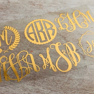 May include: Gold monogram decals in various styles. Includes a monogram within a laurel wreath, a circular monogram with scalloped edges, and several other letter combinations in elegant fonts. Perfect for personalizing items.