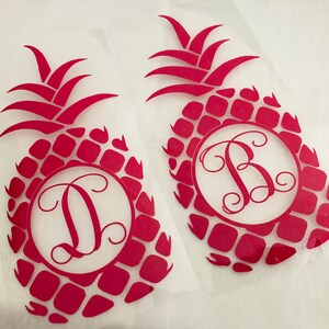 May include: Two red pineapple-shaped decals with a monogram letter inside a circle. The pineapple design features a textured pattern and a leafy crown. One decal has the letter "D", and the other has the letter "B".