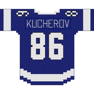 May include: A blue and white hockey jersey featuring the name "KUCHEROV" and the number "86" in white. The jersey has white detailing on the shoulders and sleeves. The design is pixelated.