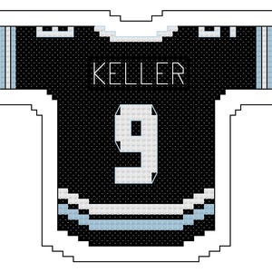 Puede incluir: Camiseta de hockey negra y blanca con el nombre "KELLER" y el número "9" en blanco. La camiseta tiene detalles en azul claro en las mangas y el dobladillo inferior. El diseño es de punto de cruz.