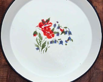 May include: A white enamel tray with a black rim and a floral design. The flowers are red and blue with green leaves. The tray is round and appears to be vintage.