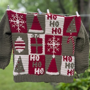 Pode incluir: Camisola de Natal feita à mão com um design de patchwork. A camisola apresenta um corpo e mangas verdes, com quadrados vermelhos, brancos e verdes. Os quadrados exibem motivos de férias como flocos de neve, árvores de Natal e o texto "HO HO HO".