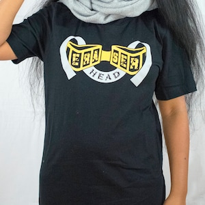 May include: Black t-shirt with a graphic of a gold chain with the words "Ear Sea Head" on it.